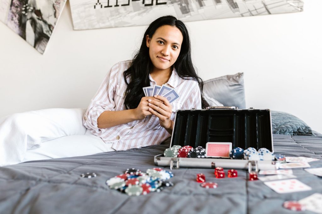 A young woman enjoys a game of poker on her bed, surrounded by cards and chips, creating a casual and playful atmosphere. — A