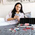 A young woman enjoys a game of poker on her bed, surrounded by cards and chips, creating a casual and playful atmosphere. — A