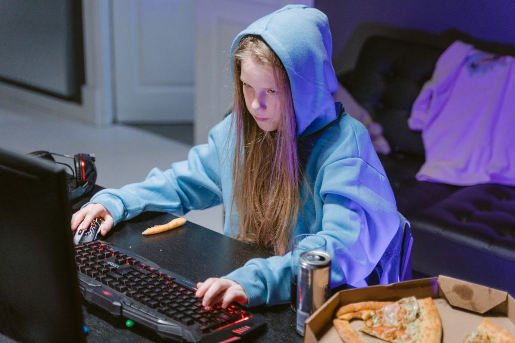 Teenage girl in blue hoodie gaming indoors with pizza and energy drink nearby. — Do You Know The Disciples Needed For Live So