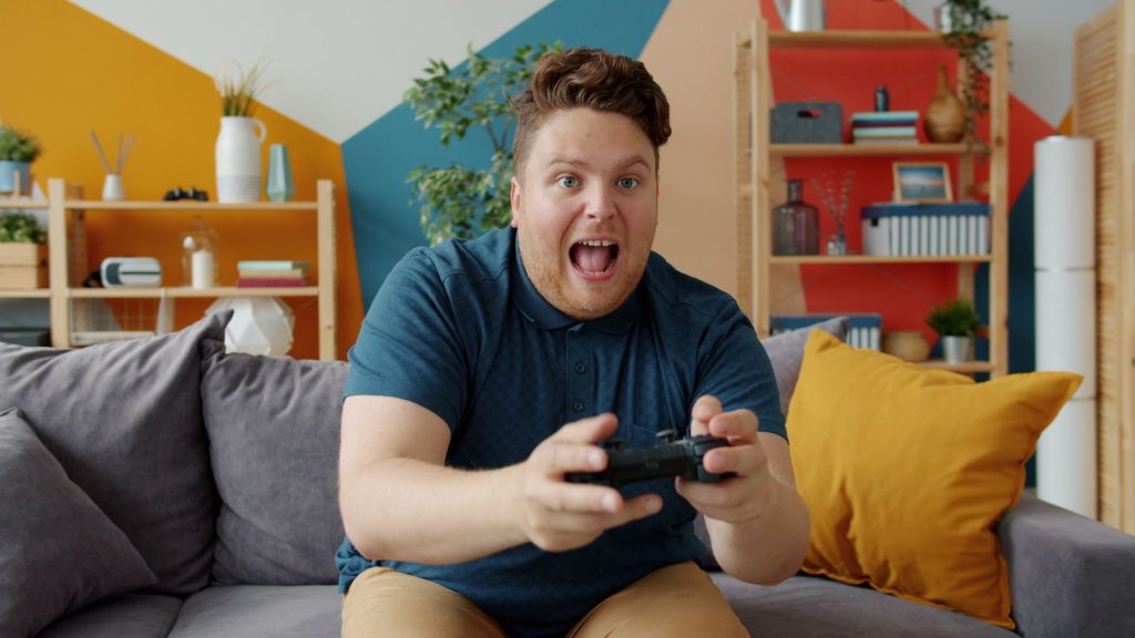 Enthusiastic adult male playing video game on console in colorful, modern living room. — Jilibet: Redefining the Art of Onlin