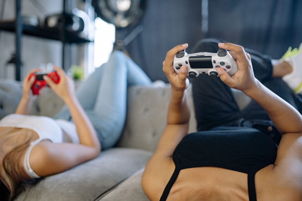 Two women relaxing and playing video games on a couch in a cozy living room. — Navigating KOITOTO Toto Macau Site: A User's G