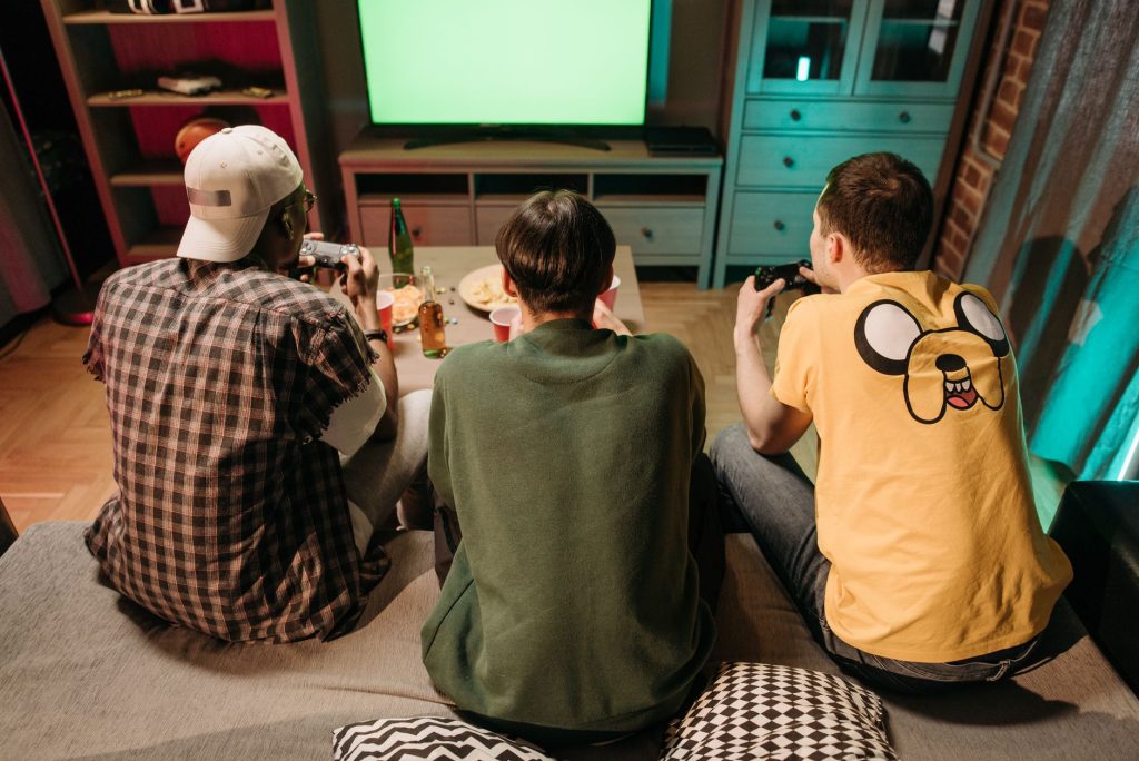 Three young men enjoying a home gaming session together, playing video games in a cozy indoors setting. — Roll Toto Site: You