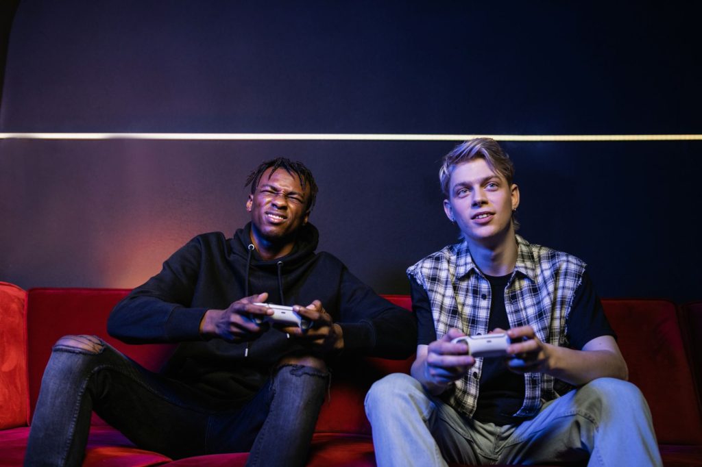 Two young men enjoying video games together on a couch, capturing leisure and friendship. — RTP Slot IDNSCORE: The Game-Chang
