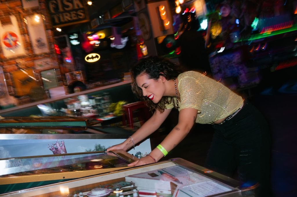 A woman cheerfully plays pinball in a vibrant, colorful arcade setting, embodying fun and entertainment. — The Best Things Ab