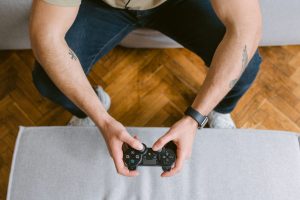 A man sitting on a couch holds a game controller, ready to play video games. — Top 4 Impressive Factors Which Have Respected