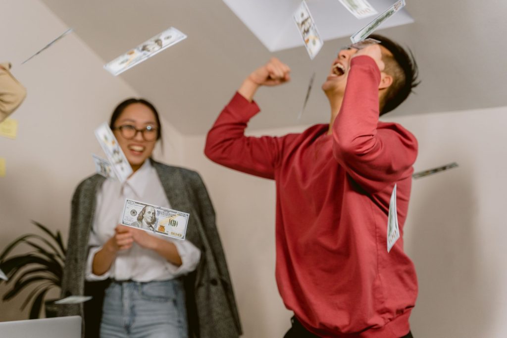 Two young adults in a room celebrating with falling dollar bills, expressing excitement and joy. — UFABET - A Passionate Spor