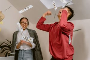 Two young adults in a room celebrating with falling dollar bills, expressing excitement and joy. — UFABET - A Passionate Spor