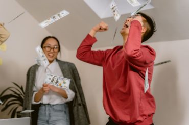 Two young adults in a room celebrating with falling dollar bills, expressing excitement and joy. — UFABET - A Passionate Spor