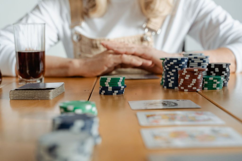 Senior woman playing poker with cards and chips on a wooden table indoors. — What advantages a novice might have online footb